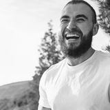 Man with a beard laughing outdoors with trees and sky in the background